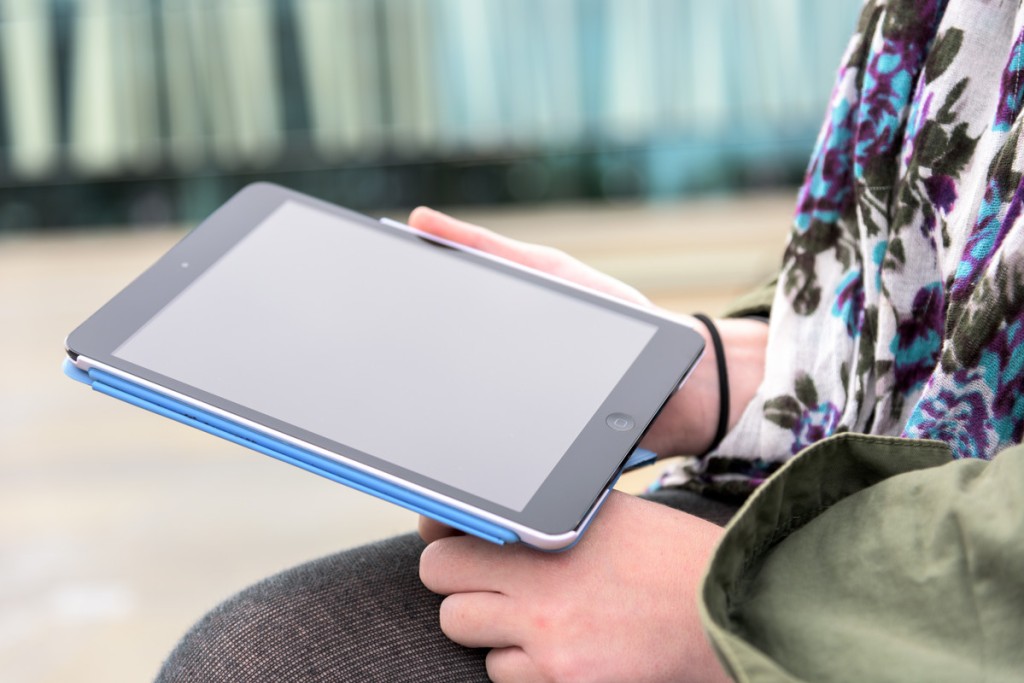 A close-up of a person holding tablet device in front of the Sir Duncan Rice Library.